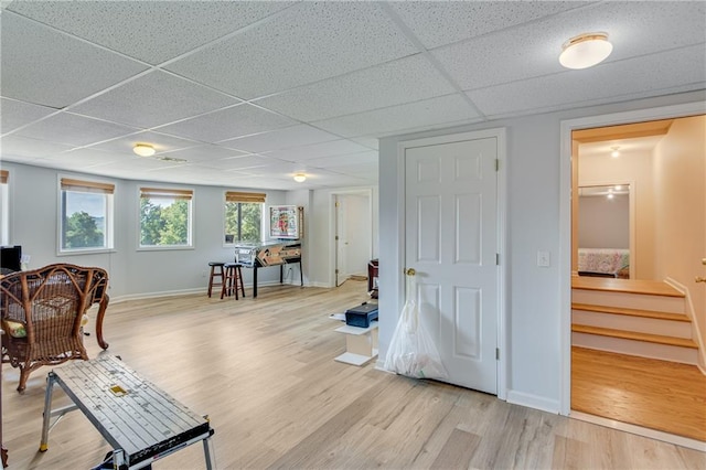 living area featuring baseboards, a paneled ceiling, light wood-style floors, and stairs