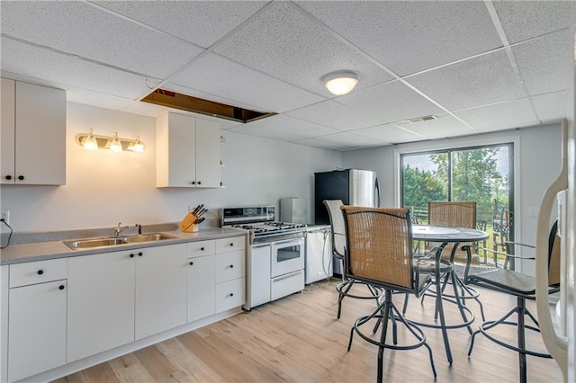 kitchen with light wood finished floors, white range with gas stovetop, freestanding refrigerator, white cabinets, and a sink