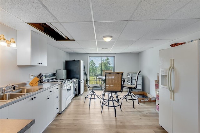 kitchen featuring a sink, white cabinets, light wood-style floors, white fridge with ice dispenser, and range with gas cooktop