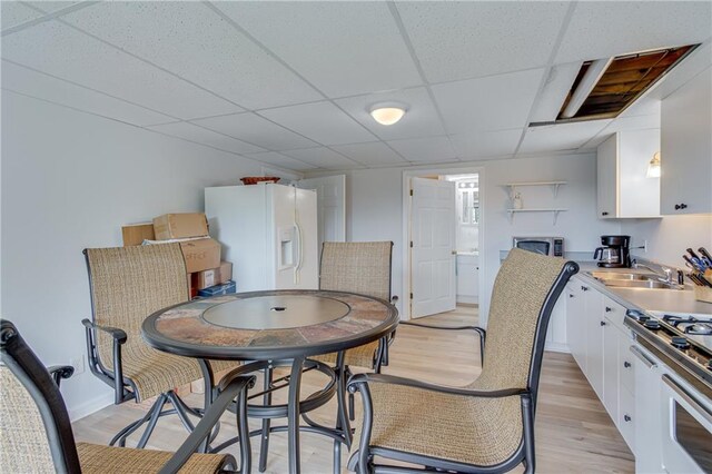 dining area featuring light wood-type flooring, a paneled ceiling, and sink