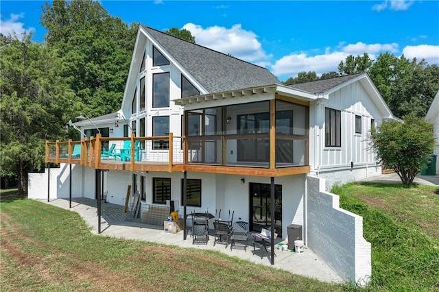 rear view of house with a shingled roof, a wooden deck, a yard, a sunroom, and a patio area