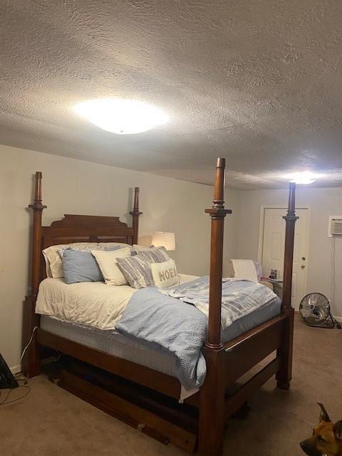 bedroom with an AC wall unit, a textured ceiling, and carpet floors