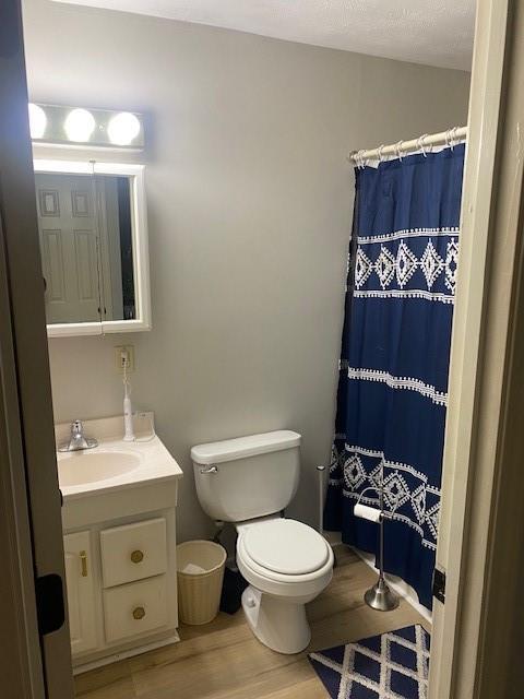 bathroom featuring hardwood / wood-style floors, walk in shower, vanity, and toilet