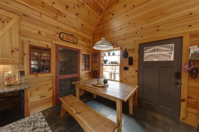 dining area featuring stone finish flooring, wood walls, and vaulted ceiling