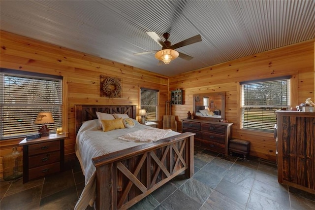 bedroom featuring stone tile floors, wood walls, and ceiling fan