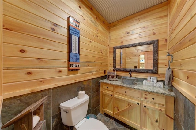 half bathroom with wooden walls, toilet, and vanity