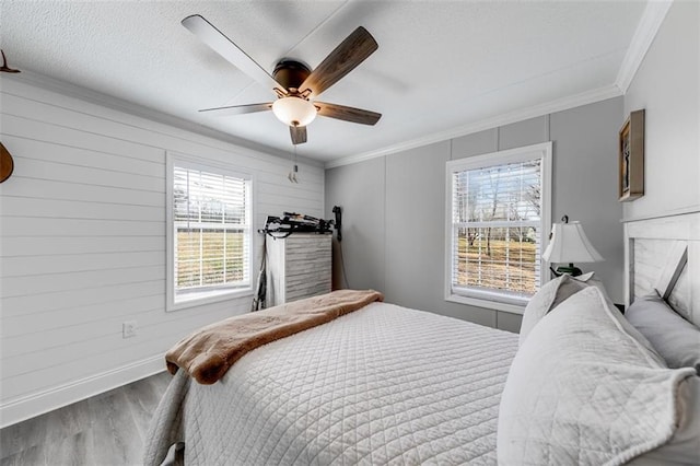 bedroom featuring a ceiling fan, wood finished floors, baseboards, ornamental molding, and a textured ceiling