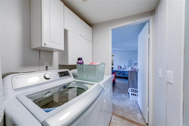 clothes washing area featuring washer and clothes dryer, cabinet space, and stone finish flooring