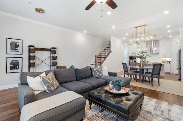 living room featuring hardwood / wood-style flooring, ornamental molding, and ceiling fan with notable chandelier