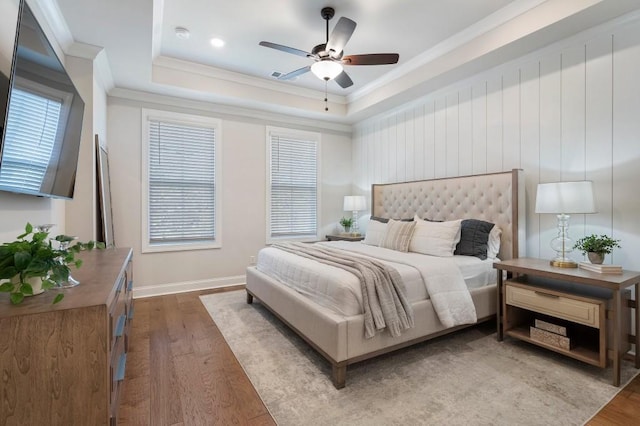 bedroom featuring a raised ceiling, wood-type flooring, crown molding, and multiple windows