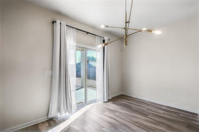 spare room featuring wood-type flooring and an inviting chandelier