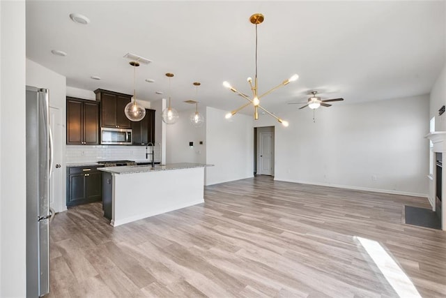 kitchen with decorative light fixtures, stainless steel appliances, an island with sink, decorative backsplash, and ceiling fan with notable chandelier