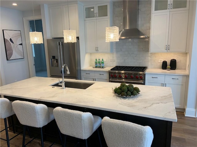 kitchen with white cabinetry, high quality appliances, a kitchen island with sink, and wall chimney range hood