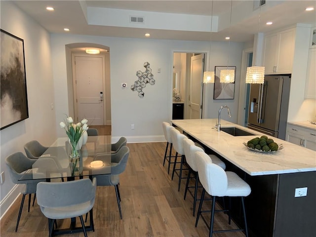 kitchen with sink, high end fridge, white cabinets, light stone countertops, and a kitchen island with sink