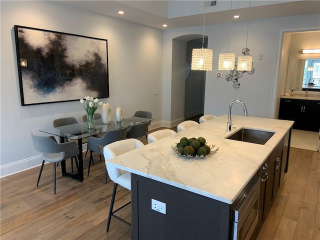 kitchen featuring sink, light stone countertops, an island with sink, and pendant lighting