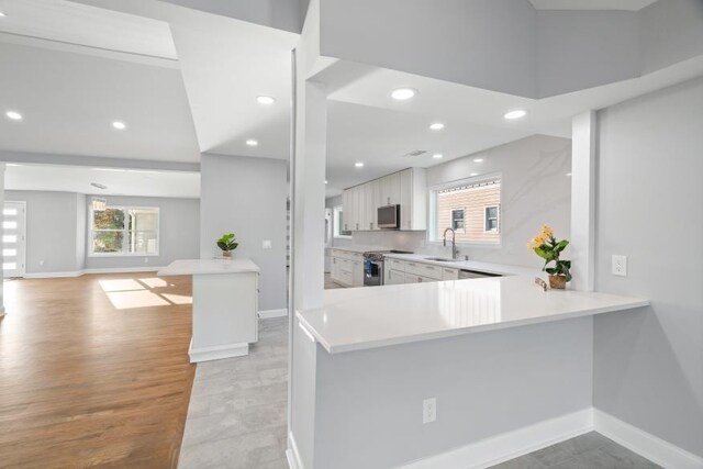 kitchen with appliances with stainless steel finishes, kitchen peninsula, a breakfast bar area, white cabinets, and light wood-type flooring