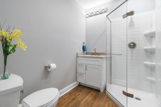 bathroom featuring wood-type flooring, vanity, toilet, and a shower with door