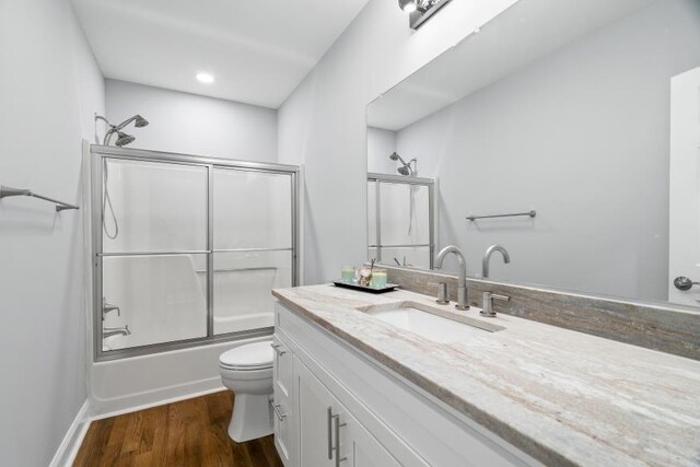 full bathroom with hardwood / wood-style floors, enclosed tub / shower combo, vanity, and toilet