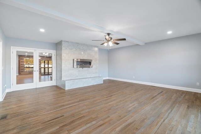 unfurnished living room with hardwood / wood-style flooring, ceiling fan, beam ceiling, a large fireplace, and french doors