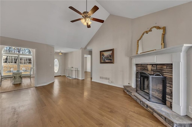 living area with visible vents, ceiling fan, wood finished floors, a stone fireplace, and high vaulted ceiling