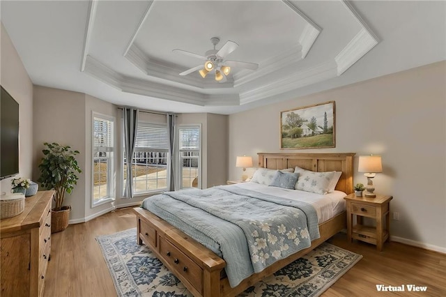 bedroom featuring light wood finished floors, a raised ceiling, ornamental molding, ceiling fan, and baseboards