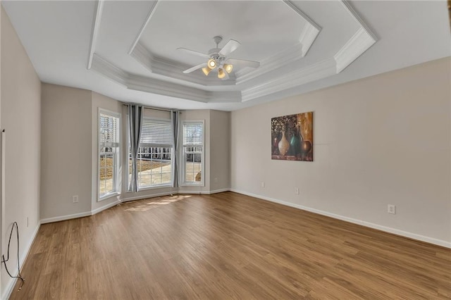 unfurnished room featuring a tray ceiling, a ceiling fan, ornamental molding, wood finished floors, and baseboards