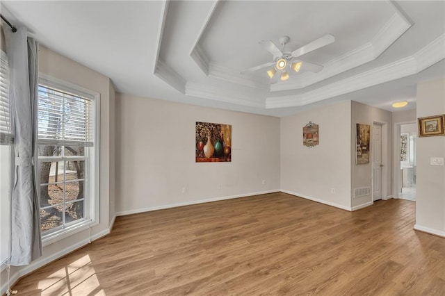 spare room featuring baseboards, a raised ceiling, a ceiling fan, crown molding, and light wood-type flooring