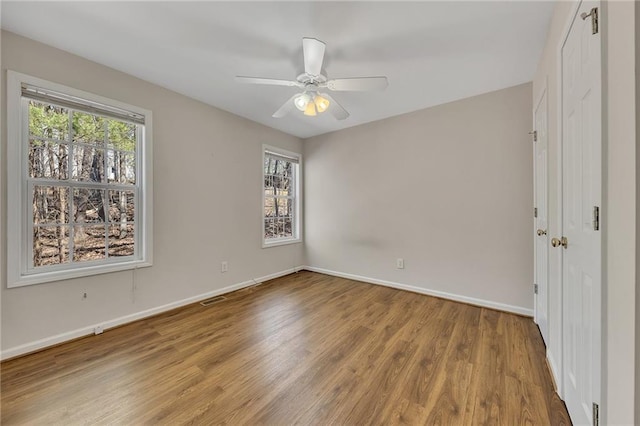 unfurnished bedroom featuring a ceiling fan, visible vents, baseboards, and wood finished floors