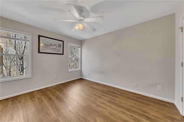 empty room featuring a wealth of natural light, baseboards, and wood finished floors