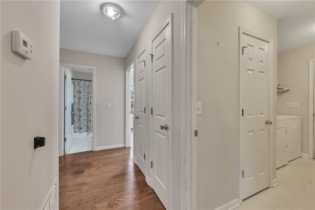 corridor featuring light wood-style flooring, visible vents, baseboards, and washer and dryer