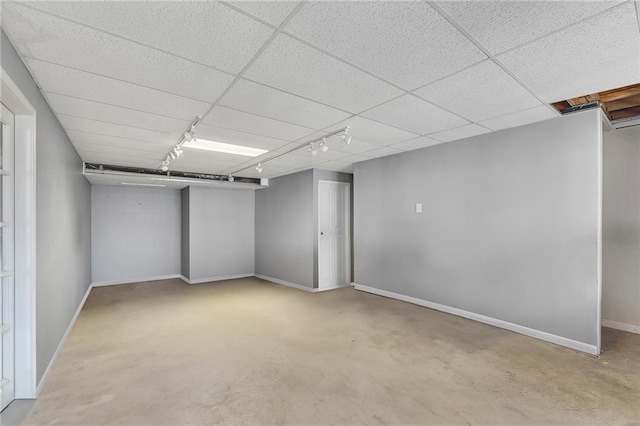 finished below grade area with a paneled ceiling, rail lighting, and baseboards