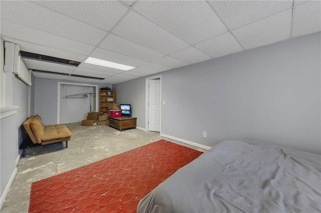 bedroom featuring concrete floors, a closet, a paneled ceiling, and baseboards