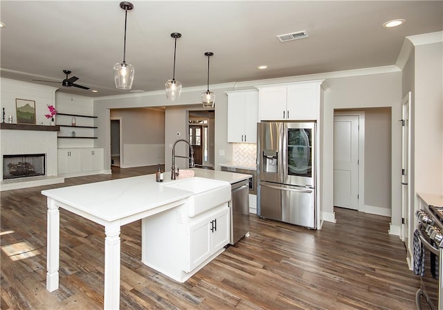 kitchen with a fireplace with raised hearth, a sink, visible vents, appliances with stainless steel finishes, and crown molding