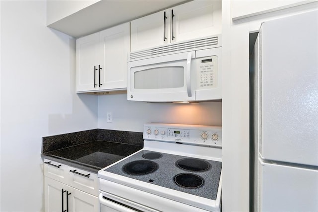 kitchen with dark countertops, white appliances, and white cabinetry