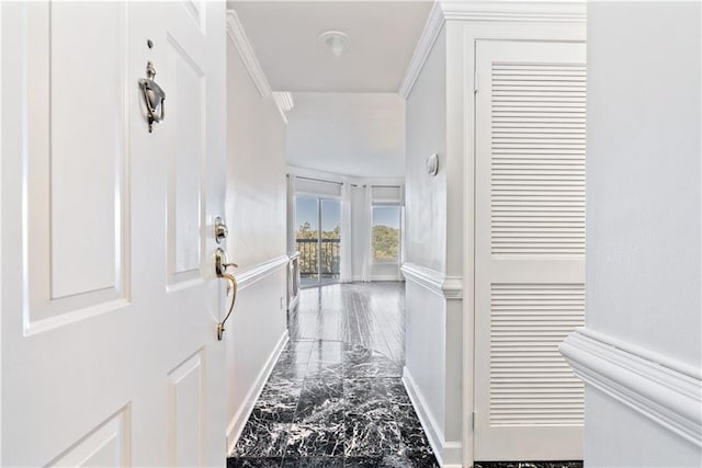 corridor with a wainscoted wall, marble finish floor, ornamental molding, and a decorative wall