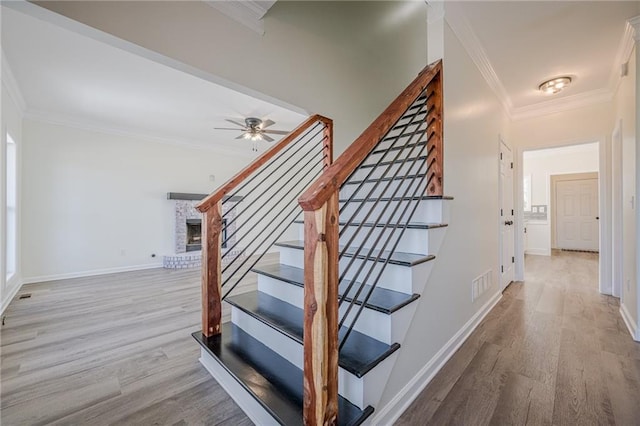 stairway with a fireplace, visible vents, ornamental molding, wood finished floors, and baseboards