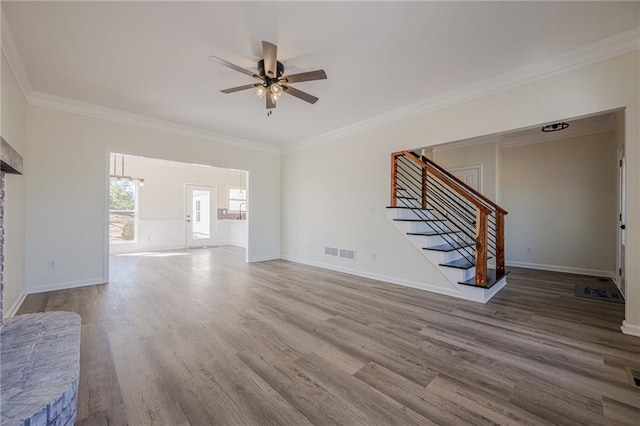 unfurnished living room featuring ceiling fan, wood finished floors, visible vents, ornamental molding, and stairway