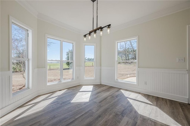 unfurnished dining area featuring plenty of natural light, ornamental molding, dark wood finished floors, and wainscoting