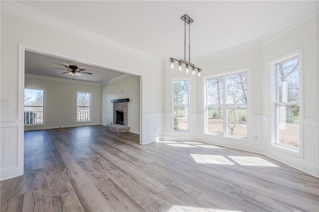 unfurnished living room with a wainscoted wall, crown molding, a brick fireplace, and wood finished floors