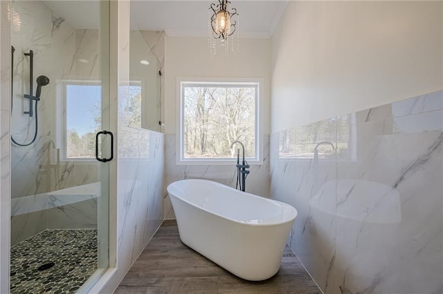 bathroom featuring wood finished floors, a soaking tub, a marble finish shower, and tile walls