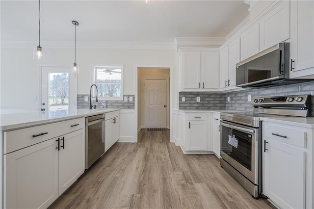kitchen featuring tasteful backsplash, appliances with stainless steel finishes, ornamental molding, a peninsula, and white cabinetry