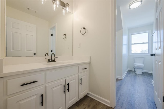 bathroom featuring baseboards, visible vents, toilet, wood finished floors, and vanity