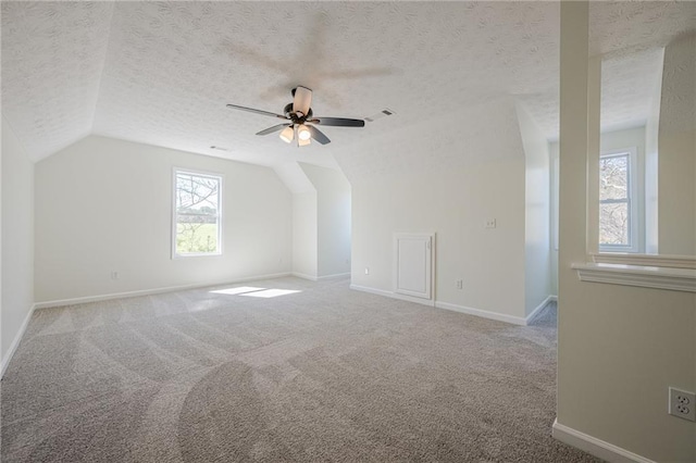 empty room with carpet floors, visible vents, vaulted ceiling, a textured ceiling, and baseboards