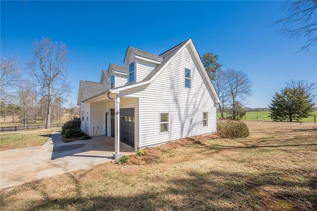 view of side of property featuring driveway, a garage, fence, and a lawn