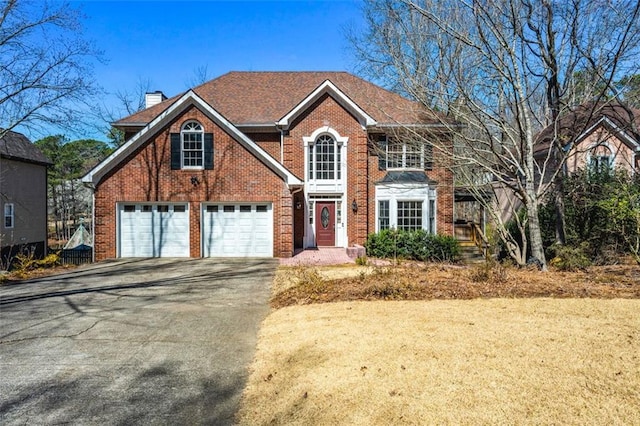 view of front of house featuring aphalt driveway, a garage, a chimney, and brick siding