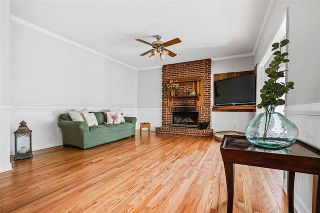 living room featuring crown molding, wood finished floors, wainscoting, and ceiling fan