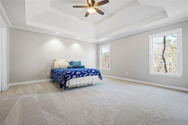 carpeted bedroom featuring a tray ceiling, baseboards, a ceiling fan, and crown molding