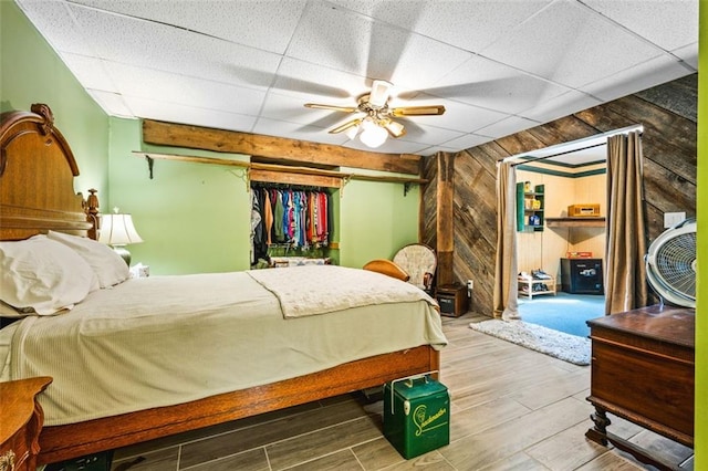 bedroom featuring a ceiling fan, a drop ceiling, wood finished floors, and wood walls