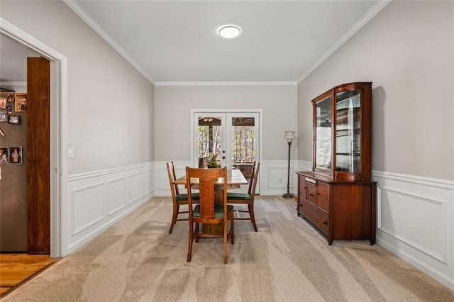 dining area featuring light colored carpet, a wainscoted wall, french doors, and ornamental molding