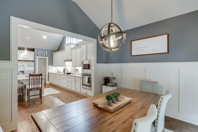 dining room featuring high vaulted ceiling, light wood-type flooring, and an inviting chandelier